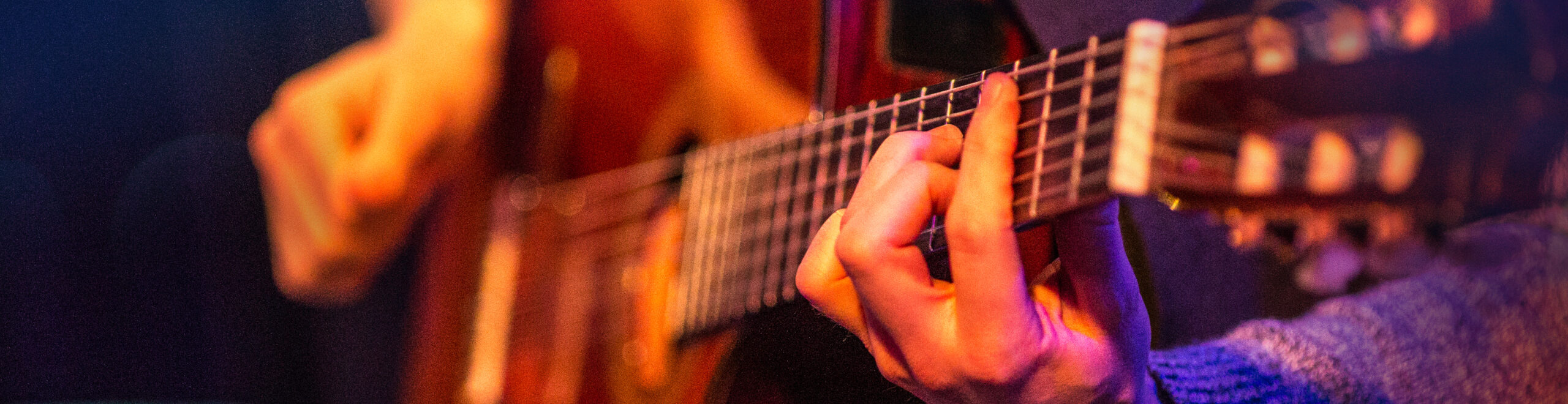 close up of a young man playing acoustic guitar in concert. focus is on the finger from the left hand. any bokeh is visible in the image